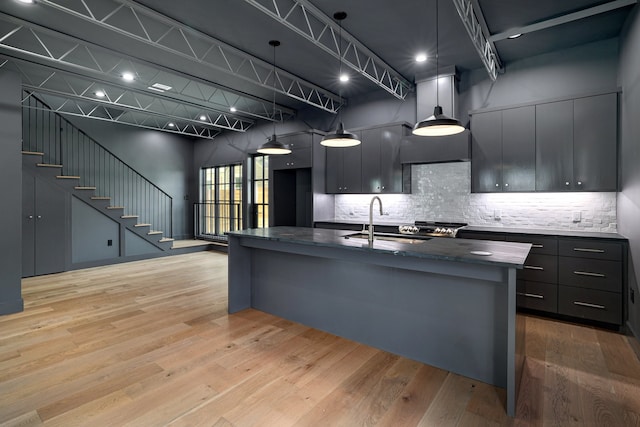 kitchen with light hardwood / wood-style floors, pendant lighting, decorative backsplash, sink, and a kitchen island with sink