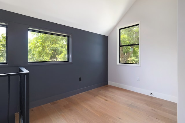 spare room featuring lofted ceiling, light wood-type flooring, and plenty of natural light