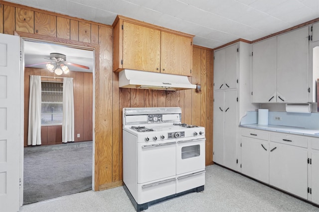 kitchen with ceiling fan, light colored carpet, wood walls, white cabinetry, and range with two ovens