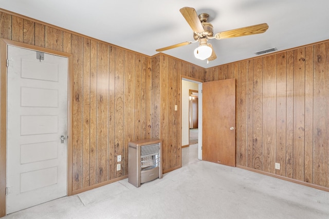 empty room featuring ceiling fan, heating unit, light carpet, and wooden walls