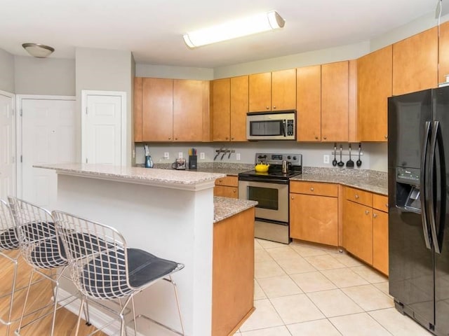 kitchen featuring a center island, a breakfast bar, light stone countertops, appliances with stainless steel finishes, and light tile patterned floors