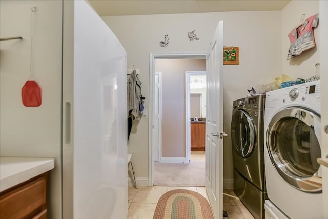 clothes washing area featuring laundry area, light tile patterned flooring, baseboards, and washing machine and clothes dryer