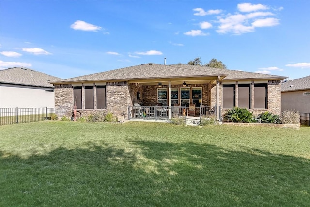 rear view of house featuring a ceiling fan, brick siding, a yard, and fence