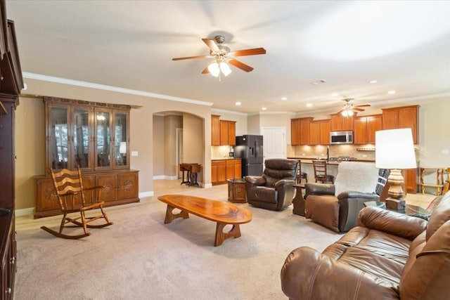 living room featuring arched walkways, ornamental molding, light carpet, and a ceiling fan