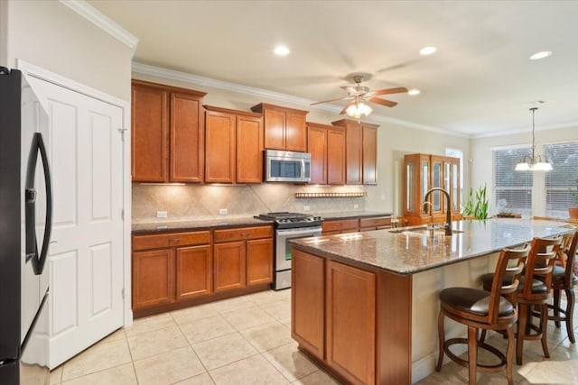 kitchen with brown cabinetry, an island with sink, hanging light fixtures, stainless steel appliances, and a sink