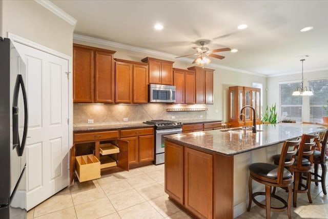 kitchen featuring stone counters, a kitchen island with sink, stainless steel appliances, hanging light fixtures, and brown cabinetry