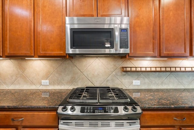 kitchen with appliances with stainless steel finishes, dark stone counters, brown cabinets, and backsplash