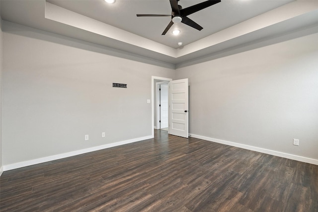 unfurnished room featuring a raised ceiling, ceiling fan, and dark wood-type flooring