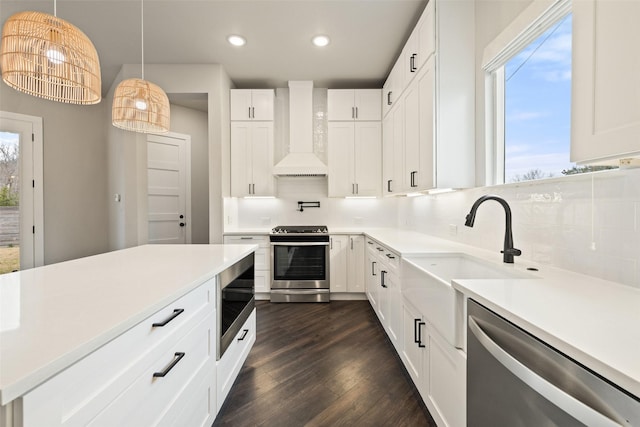 kitchen with appliances with stainless steel finishes, decorative light fixtures, white cabinetry, wall chimney range hood, and decorative backsplash