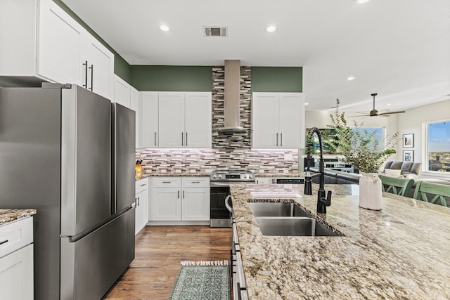 kitchen featuring appliances with stainless steel finishes, wall chimney exhaust hood, white cabinets, and sink