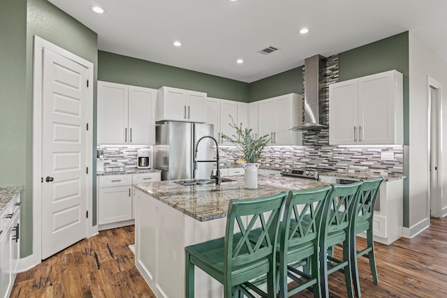 kitchen with a kitchen island with sink, wall chimney exhaust hood, sink, and light stone counters