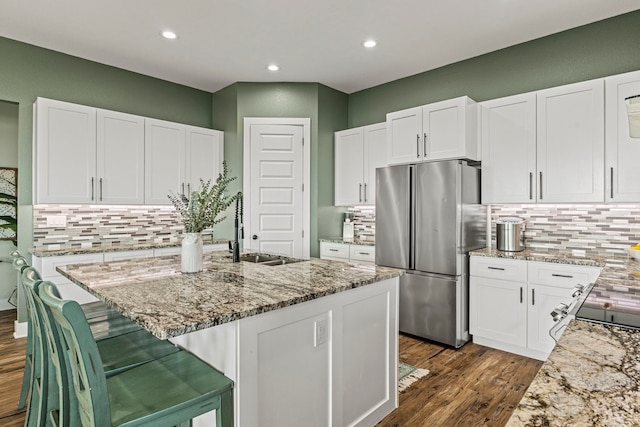 kitchen with sink, white cabinets, stainless steel fridge, and a kitchen island with sink