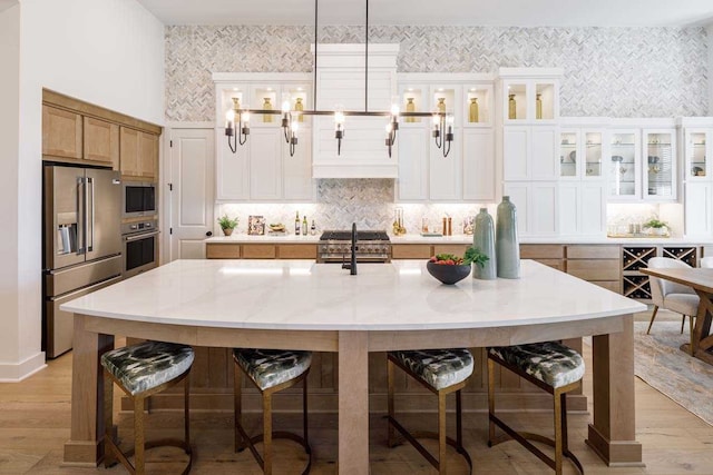 kitchen with hanging light fixtures, white cabinets, a kitchen island with sink, and high quality appliances