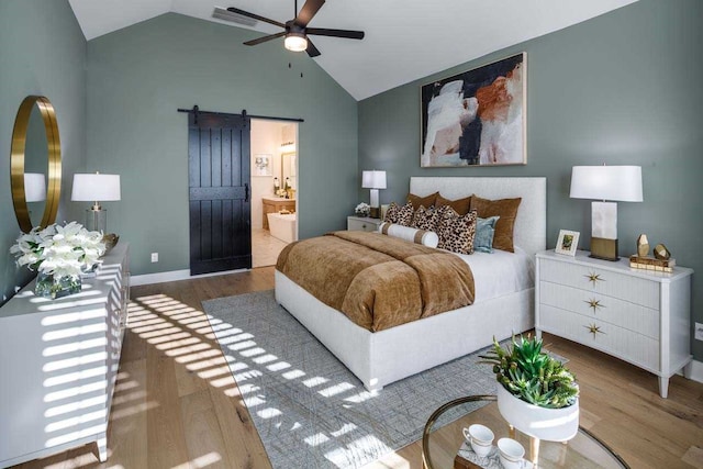 bedroom with ensuite bathroom, a barn door, ceiling fan, and hardwood / wood-style flooring