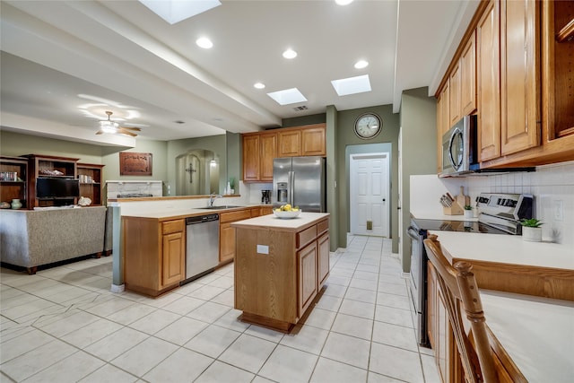 kitchen featuring kitchen peninsula, ceiling fan, appliances with stainless steel finishes, decorative backsplash, and a center island