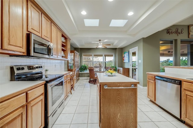 kitchen featuring light tile patterned flooring, backsplash, a center island, a tray ceiling, and stainless steel appliances