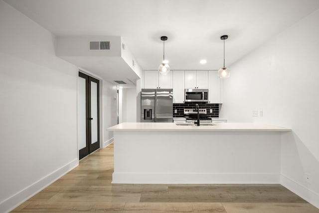 kitchen with white cabinets, decorative light fixtures, stainless steel appliances, tasteful backsplash, and kitchen peninsula