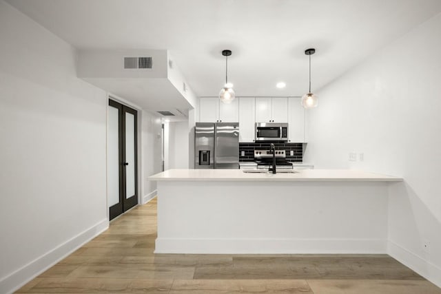909 Reinli St Unit 103, Austin, TX 78751 - kitchen featuring stainless steel appliances, a peninsula, decorative light fixtures, backsplash, and white cabinetry
