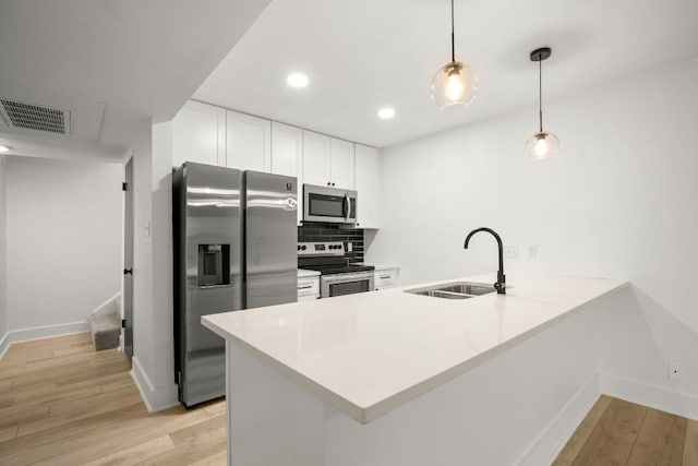 909 Reinli St Unit 103, Austin, TX 78751 - kitchen featuring appliances with stainless steel finishes, a peninsula, light wood-style flooring, white cabinets, and recessed lighting