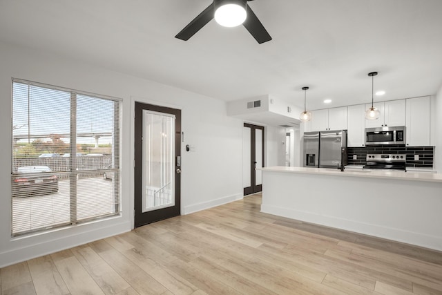 kitchen featuring white cabinetry, stainless steel appliances, backsplash, light wood-type flooring, and pendant lighting