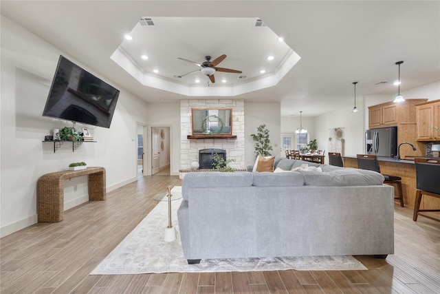 living room with a raised ceiling, ceiling fan, and a stone fireplace