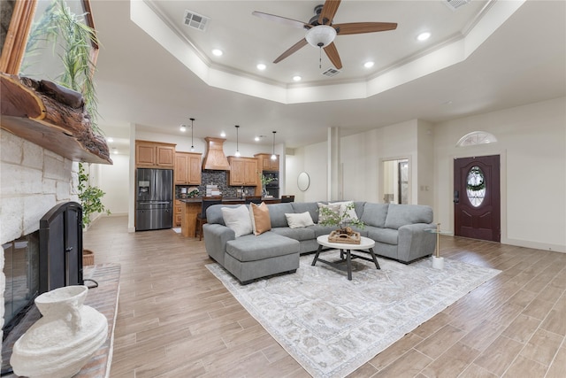 living room featuring ceiling fan, crown molding, a fireplace, and a raised ceiling