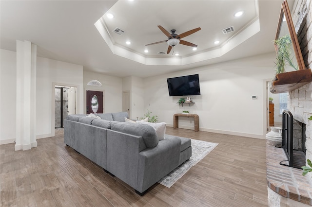 living room featuring light hardwood / wood-style floors, ceiling fan, a tray ceiling, a fireplace, and crown molding