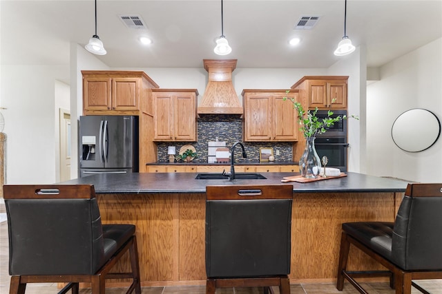 kitchen featuring decorative backsplash, premium range hood, sink, a kitchen island with sink, and fridge with ice dispenser