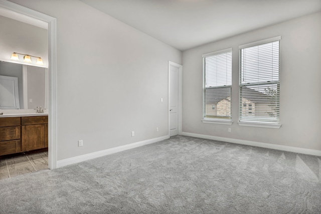 unfurnished bedroom with light colored carpet, connected bathroom, and sink