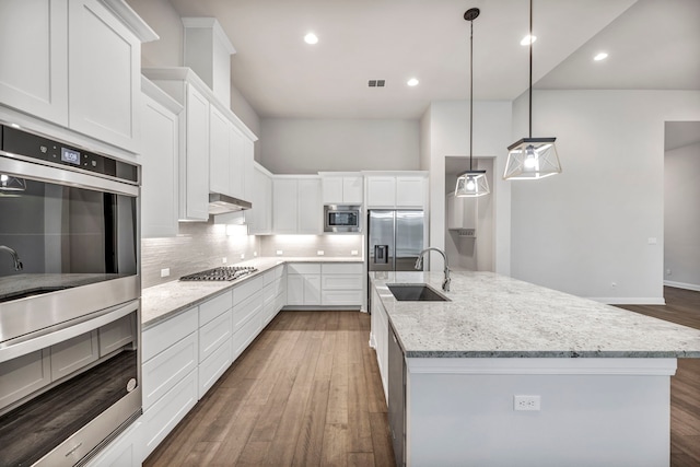 kitchen featuring appliances with stainless steel finishes, decorative light fixtures, white cabinetry, sink, and a center island with sink