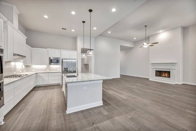 kitchen featuring ceiling fan, white cabinets, a kitchen island with sink, and built in appliances