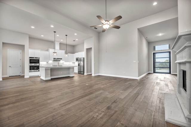 unfurnished living room featuring ceiling fan, dark hardwood / wood-style flooring, a towering ceiling, and sink