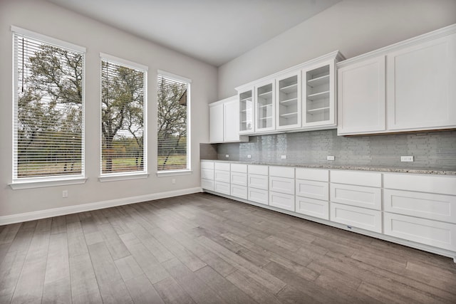 kitchen featuring light stone counters, white cabinets, tasteful backsplash, and a healthy amount of sunlight