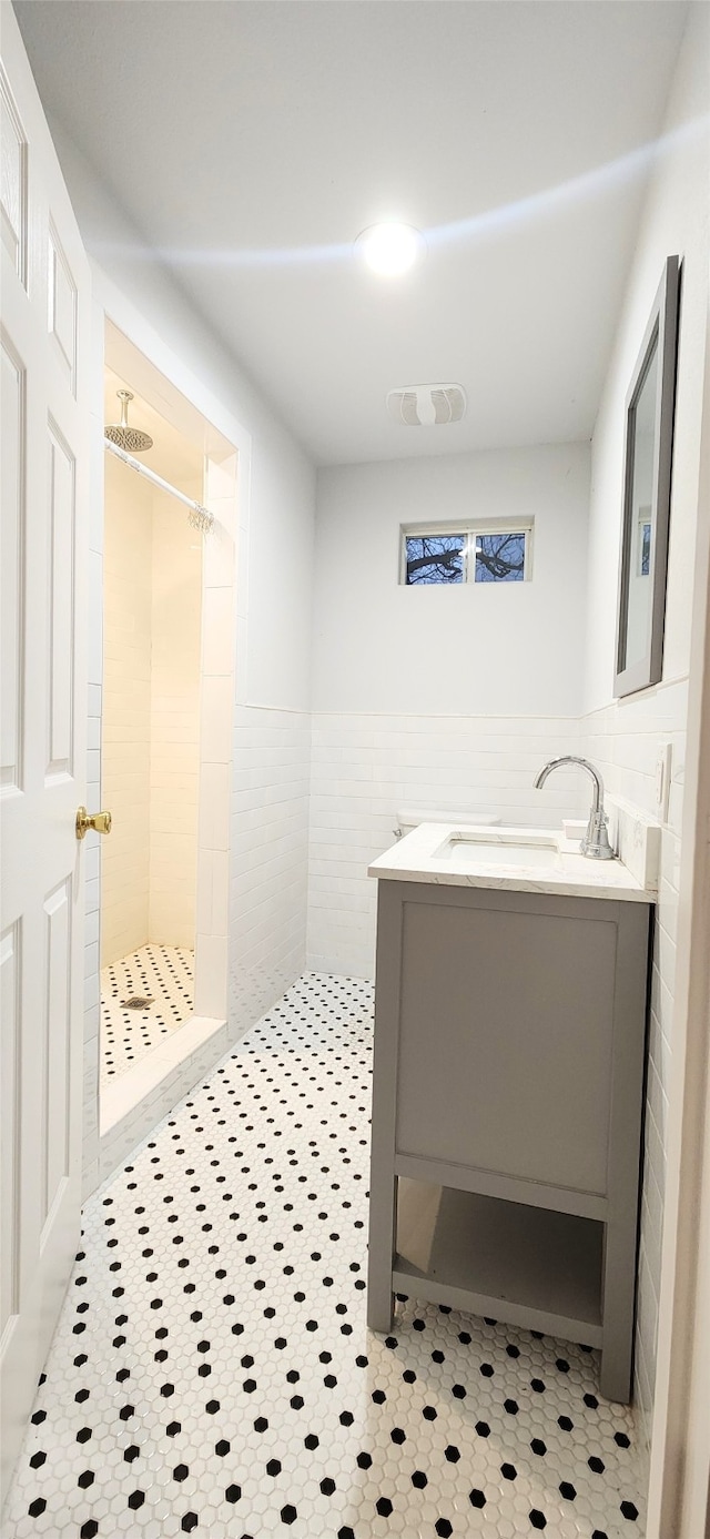 bathroom with tile walls, vanity, a tile shower, and tile patterned flooring