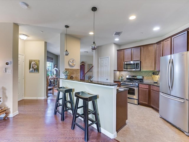 kitchen featuring appliances with stainless steel finishes, hanging light fixtures, tasteful backsplash, a kitchen bar, and kitchen peninsula