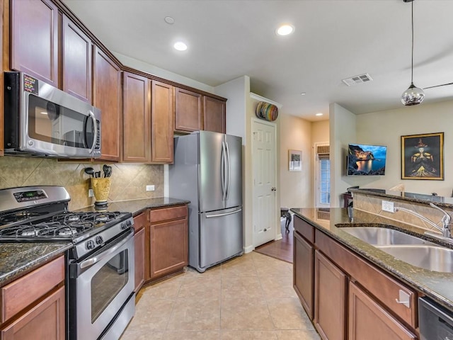 kitchen with sink, hanging light fixtures, light tile patterned floors, dark stone countertops, and appliances with stainless steel finishes