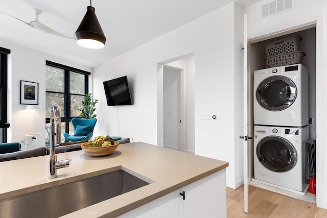 laundry area with sink, stacked washing maching and dryer, and light wood-type flooring