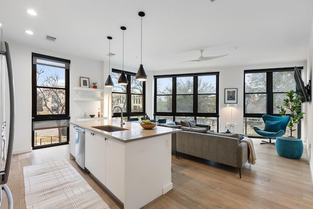 kitchen with decorative light fixtures, stainless steel dishwasher, sink, a kitchen island with sink, and white cabinets