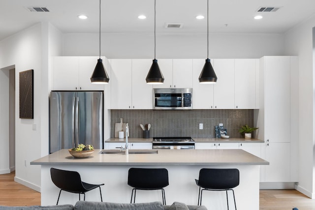 kitchen featuring hanging light fixtures, a kitchen island with sink, appliances with stainless steel finishes, and white cabinetry