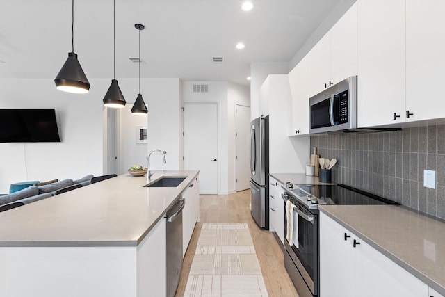 kitchen with white cabinetry, stainless steel appliances, a kitchen island with sink, hanging light fixtures, and sink