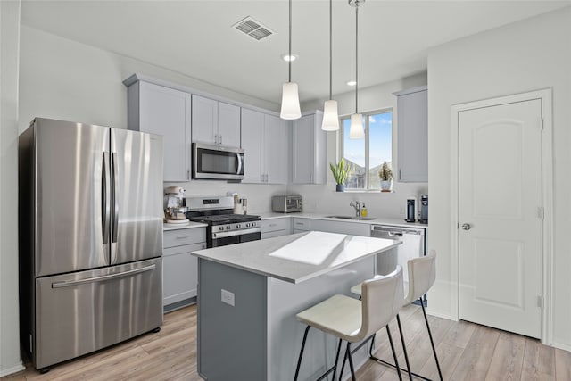 kitchen with appliances with stainless steel finishes, a kitchen island, decorative light fixtures, sink, and light wood-type flooring