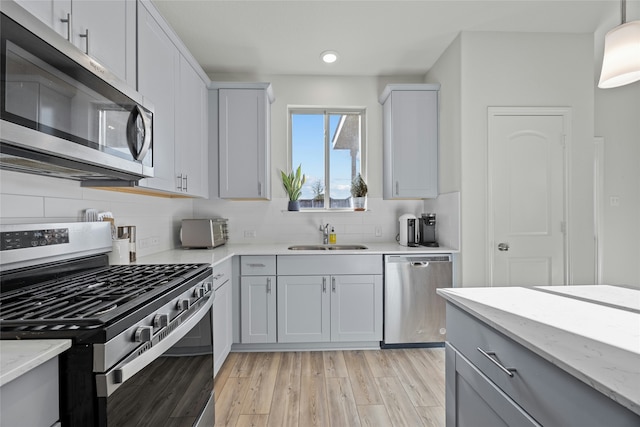 kitchen featuring light hardwood / wood-style floors, appliances with stainless steel finishes, decorative backsplash, light stone countertops, and sink