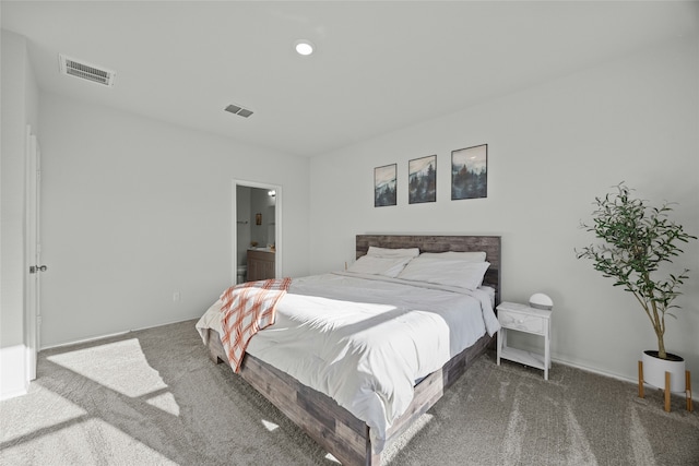 bedroom with ensuite bathroom and dark carpet