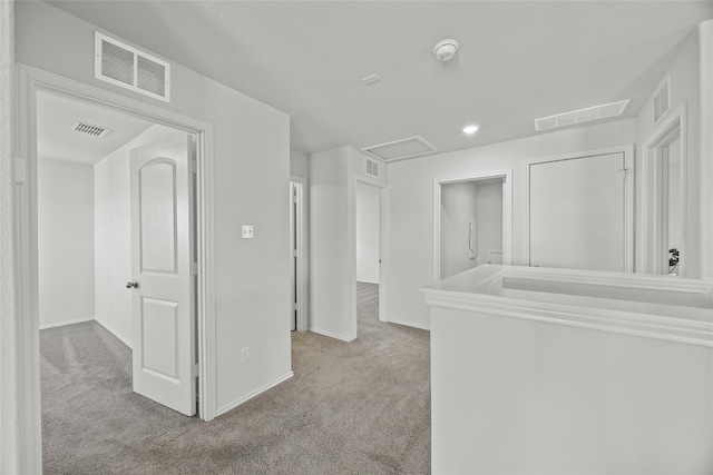 hallway with light colored carpet and a textured ceiling