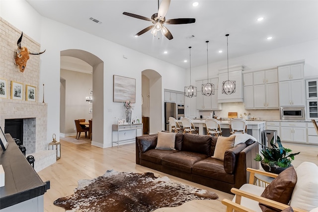 living room featuring ceiling fan, light hardwood / wood-style floors, and a brick fireplace