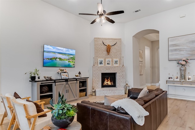 living room with a brick fireplace, light hardwood / wood-style flooring, and ceiling fan