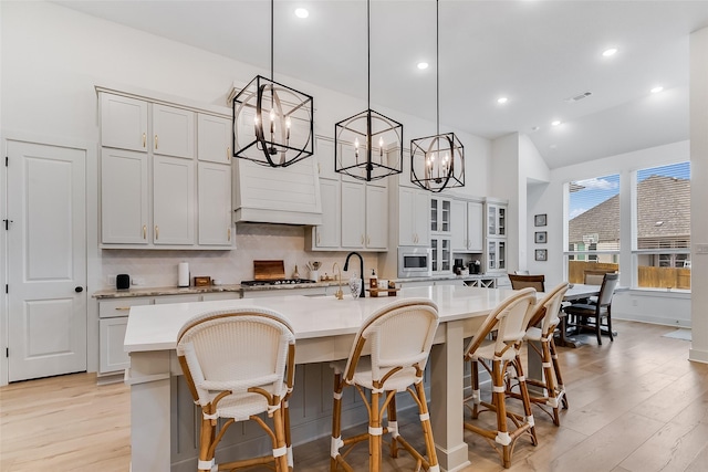 kitchen with pendant lighting, an island with sink, vaulted ceiling, a breakfast bar, and light hardwood / wood-style flooring