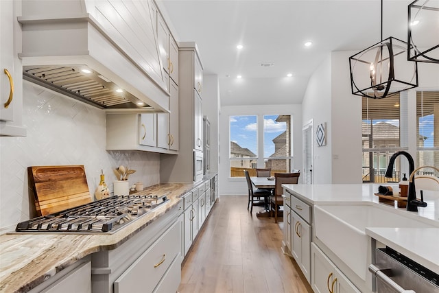 kitchen featuring pendant lighting, stainless steel appliances, tasteful backsplash, light hardwood / wood-style floors, and premium range hood