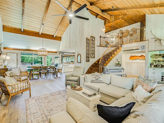 living room with wood walls, wood-type flooring, high vaulted ceiling, ceiling fan with notable chandelier, and beamed ceiling