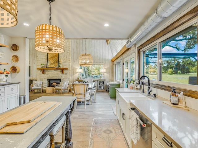 kitchen with pendant lighting, white cabinets, dishwasher, a fireplace, and light hardwood / wood-style floors